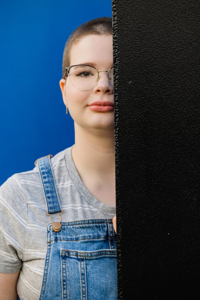 St. Louis senior dressed in blue jean overalls, with her face half hidden behind a black wall.